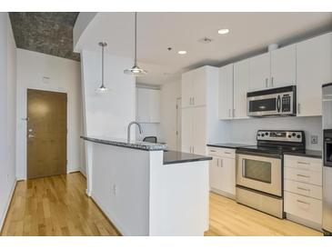This kitchen has white cabinets, stainless steel appliances, granite countertops, and hardwood floors at 943 Peachtree Ne St # 716, Atlanta, GA 30309
