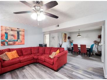 Bright living room features a ceiling fan, red couch, gray flooring and an open dining area at 6487 Northridge Way, Morrow, GA 30260