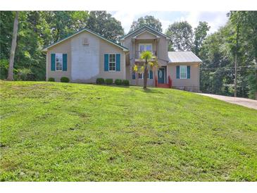 Two-story home with tan siding, teal shutters, a metal roof, and a well-manicured lawn with mature trees at 165 Country Mill Ln, Stockbridge, GA 30281