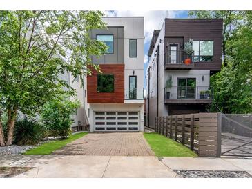 Modern, three-story home featuring a brick driveway, a two-car garage, and a mix of white, wood, and gray exterior accents at 167 Sampson Ne St, Atlanta, GA 30312
