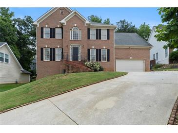 Traditional two-story brick home with a manicured lawn and a long driveway leading to a two-car garage at 2167 Merrymount Dr, Suwanee, GA 30024