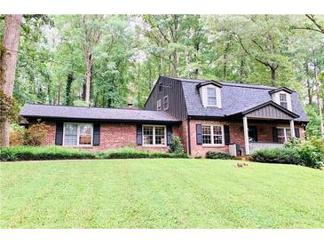 Charming brick home with a lush green lawn, mature trees, and a welcoming front porch at 1050 Lake Charles Dr, Roswell, GA 30075