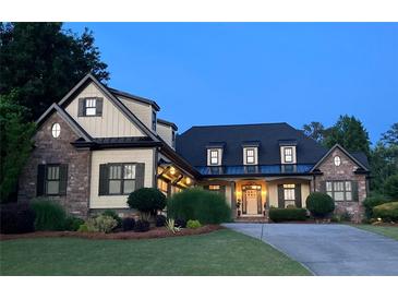 Charming home featuring manicured lawn, stone accents, and inviting entryway with a well-lit portico at dusk at 154 Gold Leaf Trail Trl, Powder Springs, GA 30127