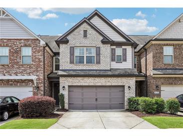 Charming brick townhome featuring a two-car garage, manicured lawn, and classic architectural details at 8215 Harlond Way, Suwanee, GA 30024