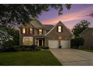 Charming brick home with manicured lawn, two-car garage, and lovely sunset in the background at 5925 Crescent Landing Dr, Cumming, GA 30028