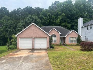 Charming brick home featuring a two-car garage and a well-maintained front lawn and lush green trees at 7513 Sugarcreek Dr, Riverdale, GA 30296