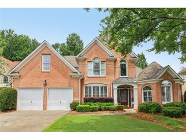 Beautiful brick home featuring a two-car garage, manicured lawn, and lush landscaping at 335 Scarborough Way, Alpharetta, GA 30022