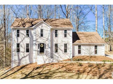 Charming two-story home with a white stucco exterior, a brown roof, and mature trees at 5050 Brownwood Dr, Powder Springs, GA 30127