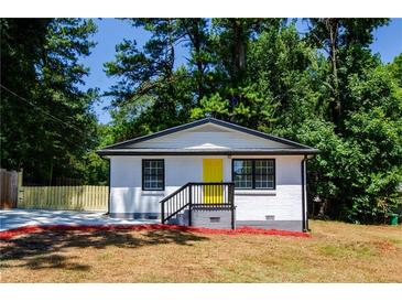 Charming home featuring a bright yellow door and freshly painted white brick, surrounded by lush greenery at 4244 Lindsey Dr, Decatur, GA 30035