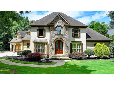 Elegant home featuring a manicured lawn, stone accents, and a welcoming arched entryway with a wood door at 2910 Creek Tree Ln, Cumming, GA 30041