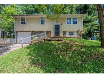 Split-level home featuring a cream-colored facade, stone accents, and an attached garage at 2242 Cherokee Valley Cir, Lithonia, GA 30058