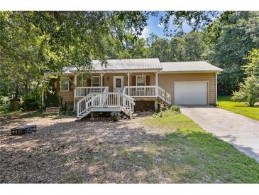Charming ranch-style home with a metal roof, front porch, and attached garage, nestled amongst lush greenery at 136 Pine St, Covington, GA 30014