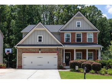 Charming two-story home featuring a two-car garage, stone accents, and a well-maintained front yard with mature trees at 6695 Grove Meadows Ln, Cumming, GA 30028