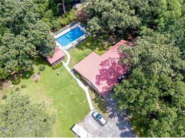Aerial view of the home with in-ground pool, green lawn, mature trees, and a red roof at 7234 Post Rd, Winston, GA 30187