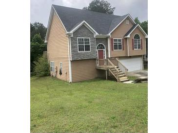 Two-story home with a well-manicured lawn, wooden porch and stairs, gray stone and tan vinyl siding at 3275 Spincaster Way, Loganville, GA 30052