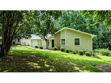 Charming single-story home featuring a stone accent wall, lawn, and a backdrop of lush trees at 3900 Ferncliff Rd, Snellville, GA 30039