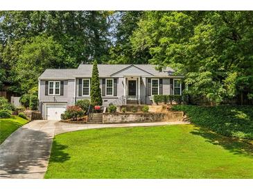 Charming home with a well-manicured front lawn, driveway, and lush landscaping with mature trees at 747 Channing Nw Dr, Atlanta, GA 30318