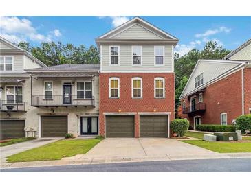 Charming townhome featuring a brick facade and individual garages, set against a backdrop of mature trees at 5933 Brookside Oak Cir, Norcross, GA 30093