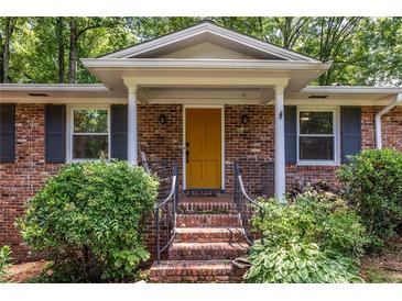 Charming brick home featuring a bright yellow front door, perfect landscaping, and covered porch at 1393 Sagewood Cir, Stone Mountain, GA 30083