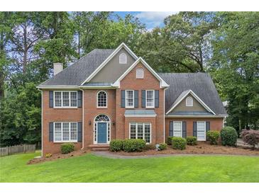 Charming brick two-story home with a blue front door, a manicured lawn, mature trees, and dark shutters at 992 Marbury Sw Ct, Marietta, GA 30064