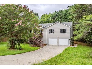 Charming home featuring a two-car garage, inviting staircase, and blossoming tree in a lush, green lawn at 49 Sweetwater Ct, Powder Springs, GA 30127