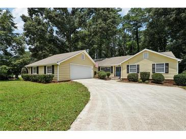 Charming yellow home featuring an attached garage, well-maintained lawn, and lengthy driveway at 2466 Country Club Dr, Conyers, GA 30013