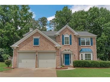 Charming brick home featuring a manicured lawn, two-car garage, and beautiful, bright blue front door and matching shutters at 5077 Wellisford Ct, Suwanee, GA 30024