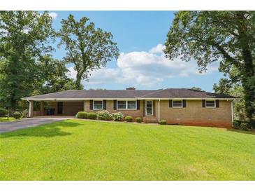 Ranch-style home with a brick facade, manicured lawn, and mature trees on a sunny day at 3212 Georgian Woods Cir, Decatur, GA 30034
