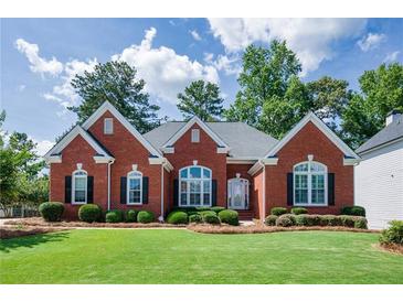 Charming red brick home with a manicured lawn, decorative windows, and lush landscaping at 205 Finsbury Park Ct, Suwanee, GA 30024