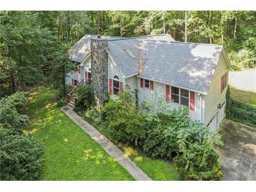Charming home exterior featuring a stone chimney, red shutters, and lush landscaping in a wooded setting at 1252 Grist Mill Dr, Acworth, GA 30101