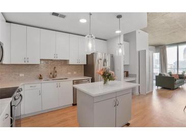 Bright kitchen features stainless appliances, white cabinets, quartz counters, kitchen island, and hardwood floors at 860 Peachtree St # 1103, Atlanta, GA 30308