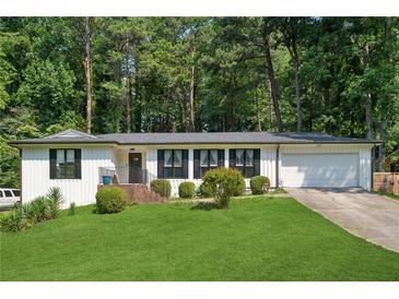 Charming single-story home with a well-manicured lawn, mature trees, and an attached garage at 5360 Fieldgreen Dr, Stone Mountain, GA 30088