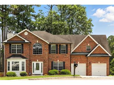 Charming two-story red brick home with a two-car garage, manicured landscaping, and mature trees at 5745 Crystal Springs Way, Powder Springs, GA 30127