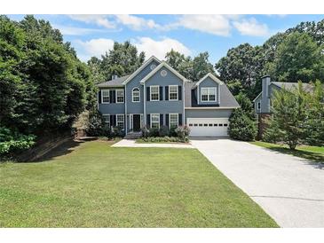 Charming two-story home with a well-manicured lawn, a long driveway, and lush landscaping at 5176 Shotwell St, Woodstock, GA 30188
