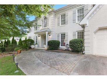 Elegant white brick home with gray shutters, complemented by a meticulously paved driveway and lush landscaping at 7045 Hunters Ne Knl, Sandy Springs, GA 30328