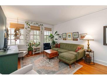 Bright living room featuring hardwood floors, a plush sofa, and sunlit windows adorned with hanging plants at 1166 Virginia Avenue Ne Ave # 8, Atlanta, GA 30306