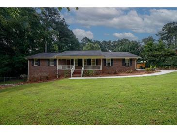 Charming brick home featuring a welcoming front porch, lush green lawn, and mature trees creating a serene setting at 2202 Springdale Dr, Snellville, GA 30078