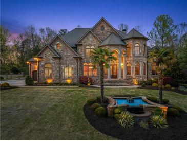 Elegant stone home with manicured lawn, water feature and palm trees at dusk at 1310 Settles Rd, Suwanee, GA 30024