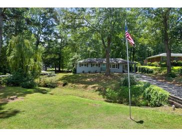Charming single-story home with a well-manicured lawn, mature trees and American flag in a wooded setting at 506 Bolijeri Blvd, Villa Rica, GA 30180