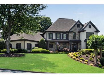 Beautiful two-story home with a manicured lawn, stone accents, and a welcoming front porch with lush, mature landscaping at 5995 Ettington Dr, Suwanee, GA 30024
