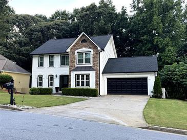 Charming two-story home boasts a combination of stone and white siding, complemented by a black garage door and manicured landscaping at 2798 Beddington Way, Suwanee, GA 30024