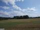 View of land with sparse grass, a tree line in the distance, and blue skies with puffy white clouds above at 0 Hawkins Academy Rd, Social Circle, GA 30025