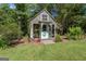 Charming outbuilding with decorative trim and a welcoming front entrance surrounded by lush greenery at 3806 Bill Gardner Pkwy, Locust Grove, GA 30248