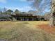 A rear exterior view of the home with green siding, mature trees, and a large grassy yard at 107 Stratford Ct, Peachtree City, GA 30269