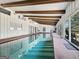 An indoor pool with exposed wood rafters, white ceiling and walls, and multiple sliding glass doors to the outside at 107 Stratford Ct, Peachtree City, GA 30269