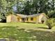 Charming home featuring a stone accent wall and yellow siding nestled among mature trees and a well-manicured lawn at 1327 Highway 54 E, Fayetteville, GA 30214