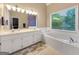 Bright bathroom featuring a soaking tub, double vanity, and large window overlooking a green view at 9135 Woodhaven Way, Mcdonough, GA 30253