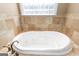 Close-up of a large, white jetted tub featuring tile surround, a glass block window, and bronze faucet at 401 Robinson Rd, Peachtree City, GA 30269