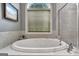 Close up of an oval soaking tub in bathroom with a window and a tiled surround at 115 Foxford Run, Tyrone, GA 30290