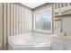 Bathroom with a whirlpool tub with tile surround, wallpaper, window with blinds and white cabinets at 123 Stratmore Pl, Stockbridge, GA 30281